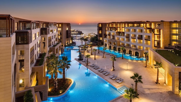 Un hotel con piscina central, varios balcones y vistas al mar al atardecer.