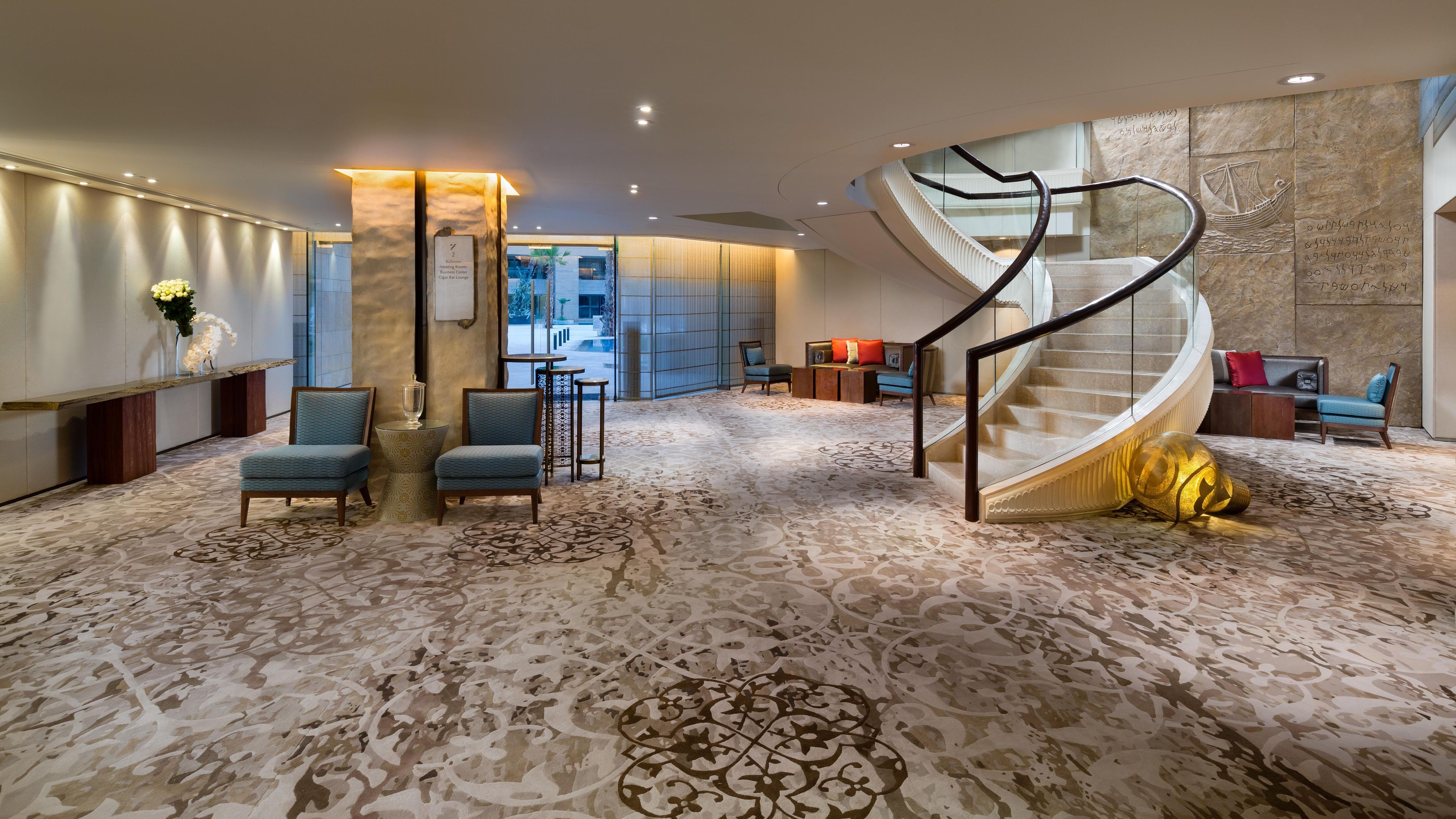 A spacious lobby with a marble floor, a spiral staircase, seating areas, and a reception desk.
