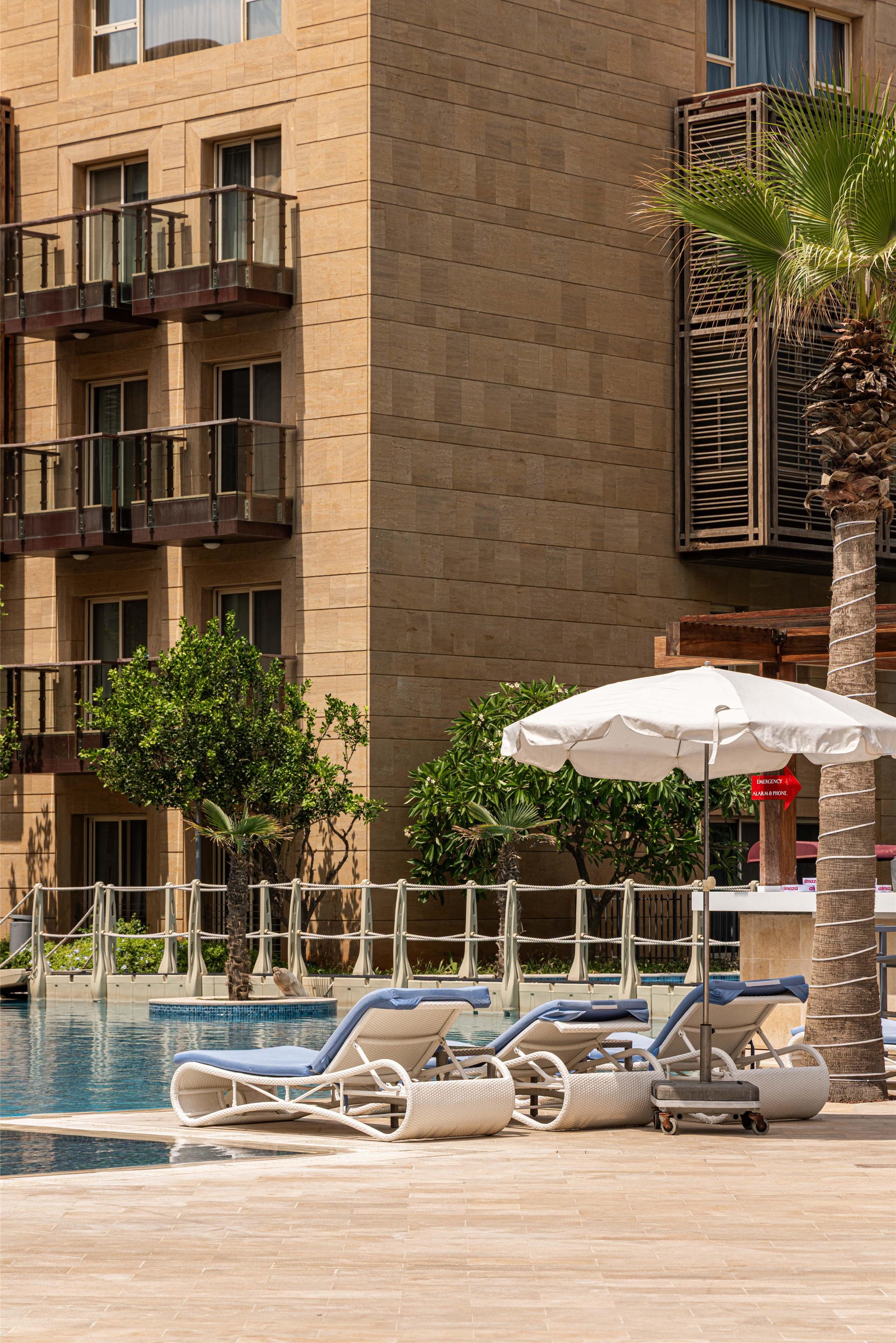 A pool area with lounge chairs and umbrellas, surrounded by a building with a brick facade and balconies.