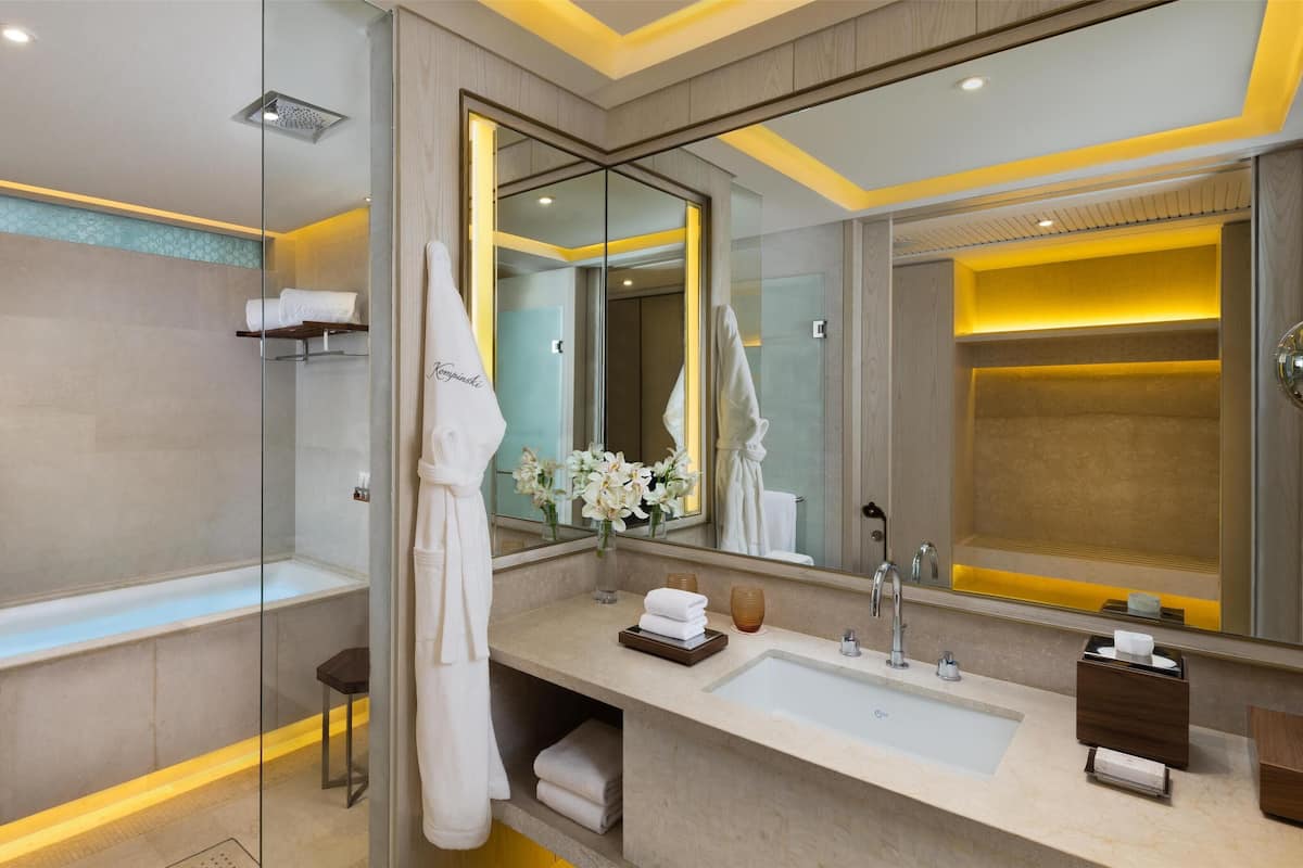 Un baño moderno con cabina de ducha acristalada, un espejo grande y un tocador con lavamanos y toallero.