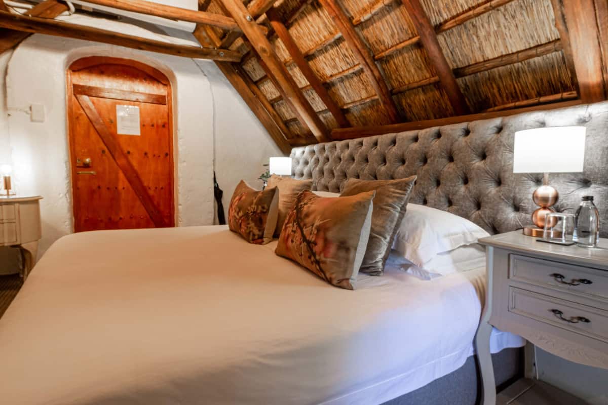 A bedroom with a large bed, wooden ceiling beams, and a nightstand with a lamp.