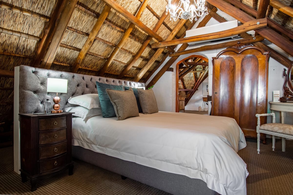 A bedroom with a large bed, a nightstand, a wooden wardrobe, and a chandelier.