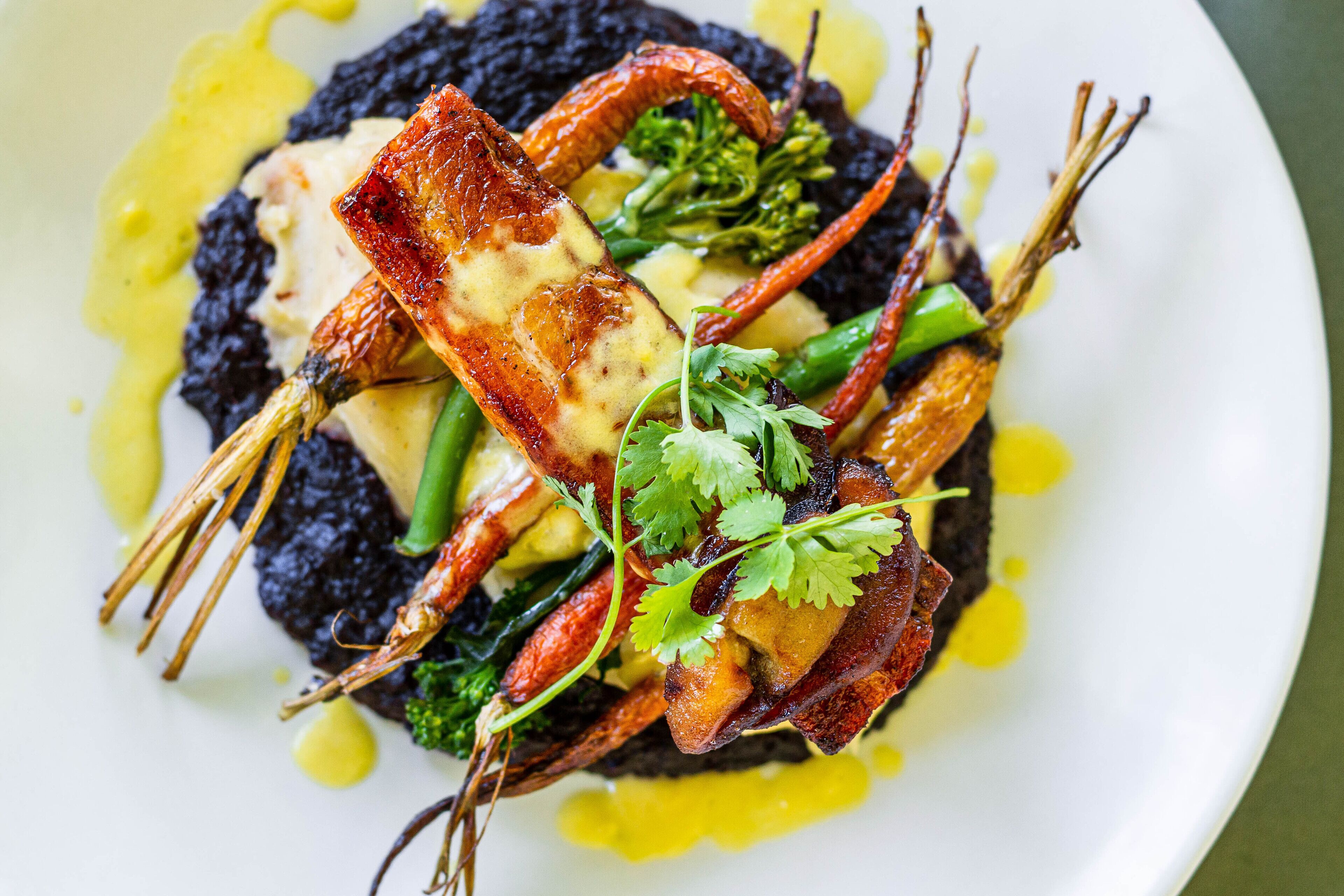 Un plato de comida con mariscos, vegetales de hoja verde y una base oscura.