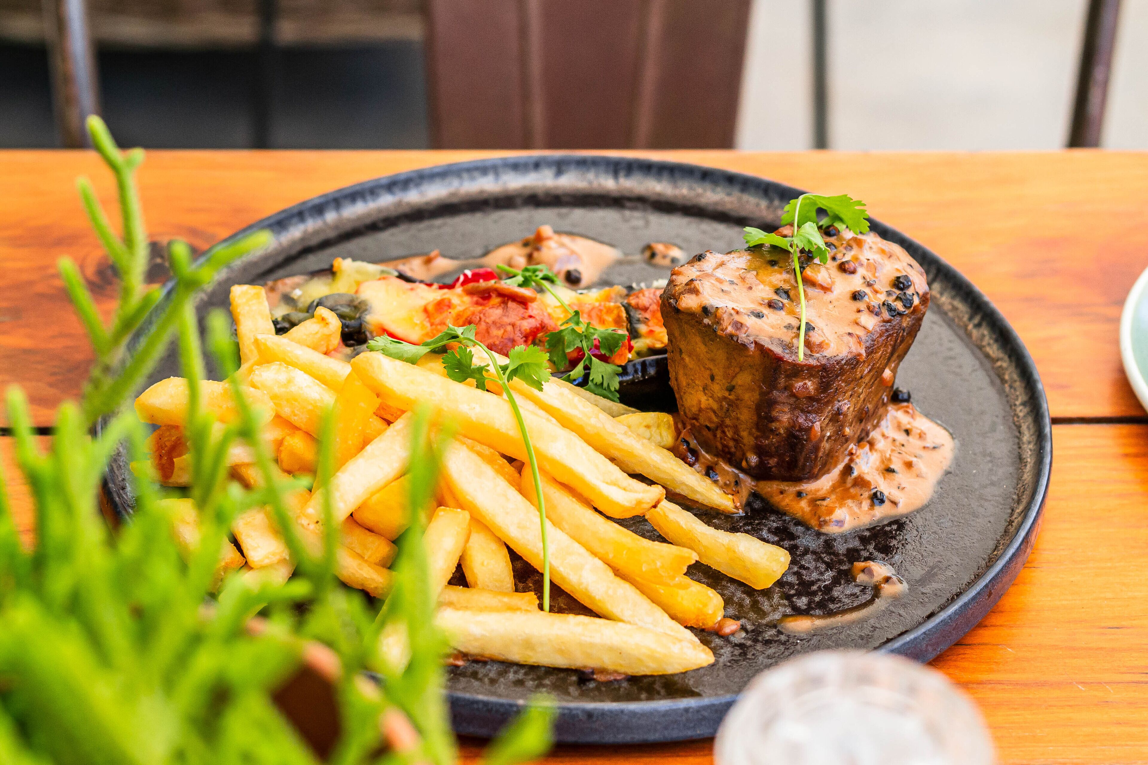 A plate of food with steak, fries, and a sauce, served on a black plate.