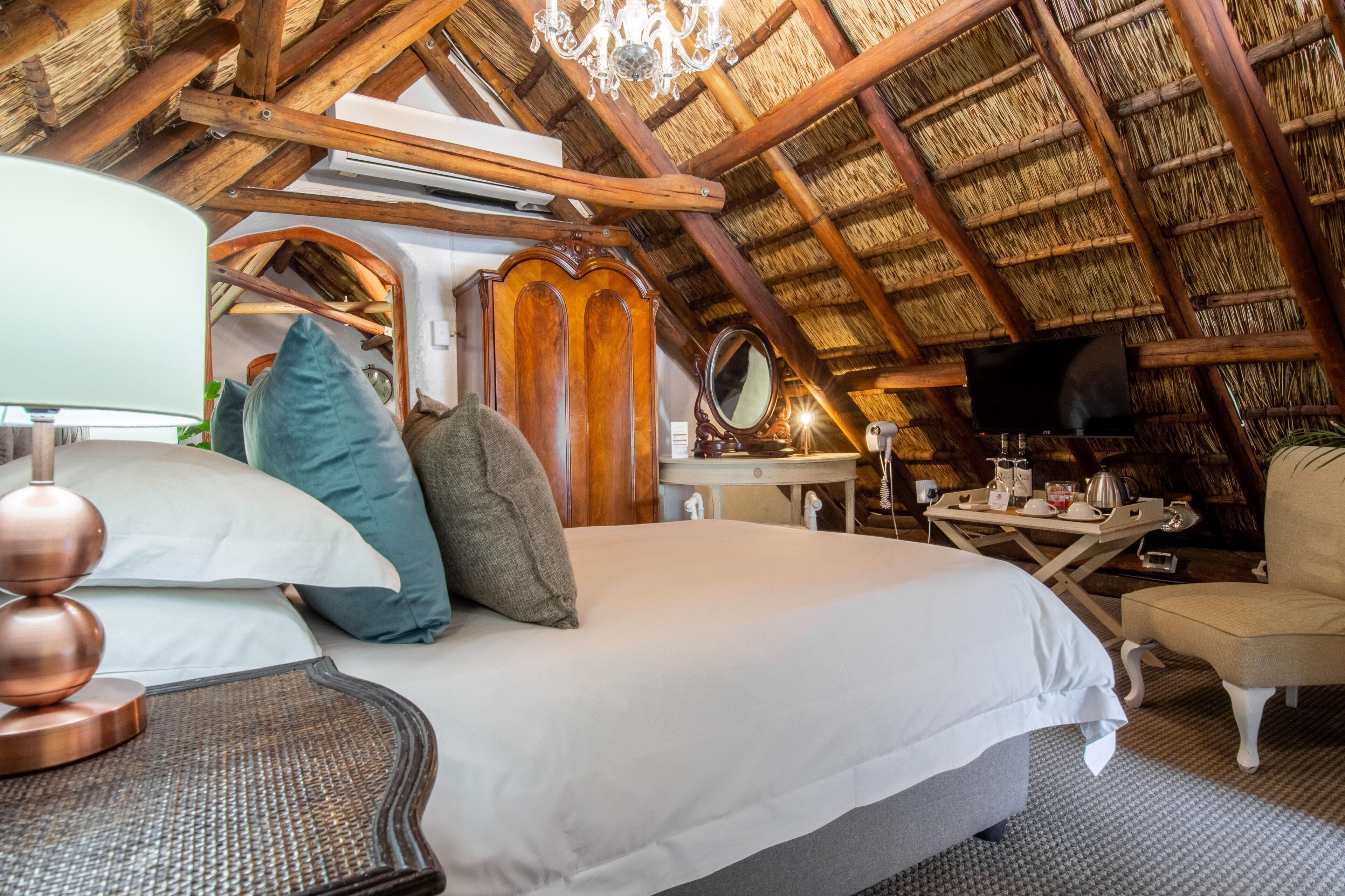 A cozy room with a bed, a chair, a table with a TV, and a chandelier.