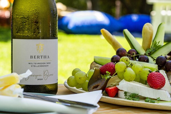 A bottle of wine, a plate with cheese, grapes, and strawberries, and a knife on a table. - Weltevreden Estate (Stellenbosch)