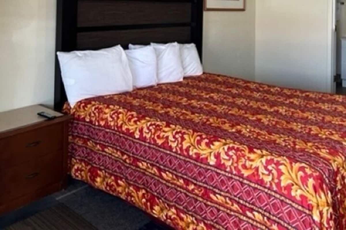 A hotel room with a large bed, a wooden nightstand, a framed picture on the wall, and a door to the right.