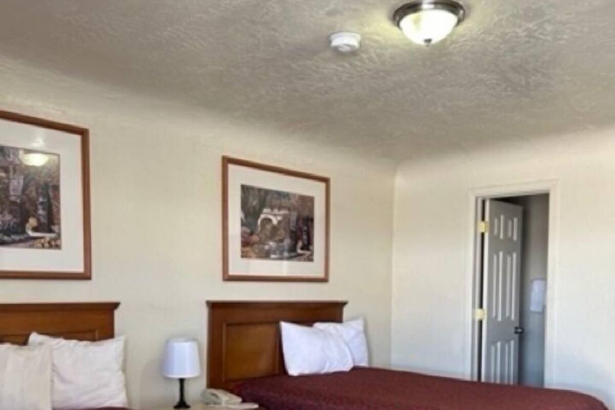 A hotel room with two beds, each with a headboard and a bedside table. There are framed pictures on the wall above the beds.