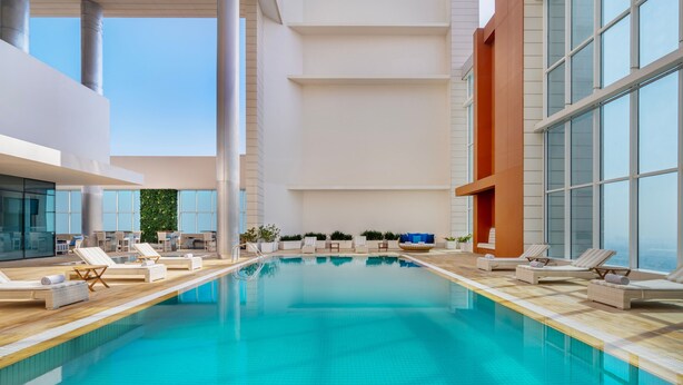 Una piscina interior moderna con agua azul cristalina, rodeada de sillones de descanso y plantas en macetas.