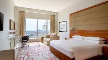 Una habitación de hotel con una cama grande, un escritorio con silla, un televisor y vistas a la ciudad.