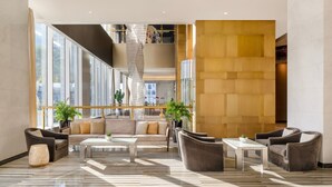 Un lobby espacioso de diseño moderno, con una zona de estar central con sofás y sillones, una escalera y ventanas amplias con vistas a la ciudad.
