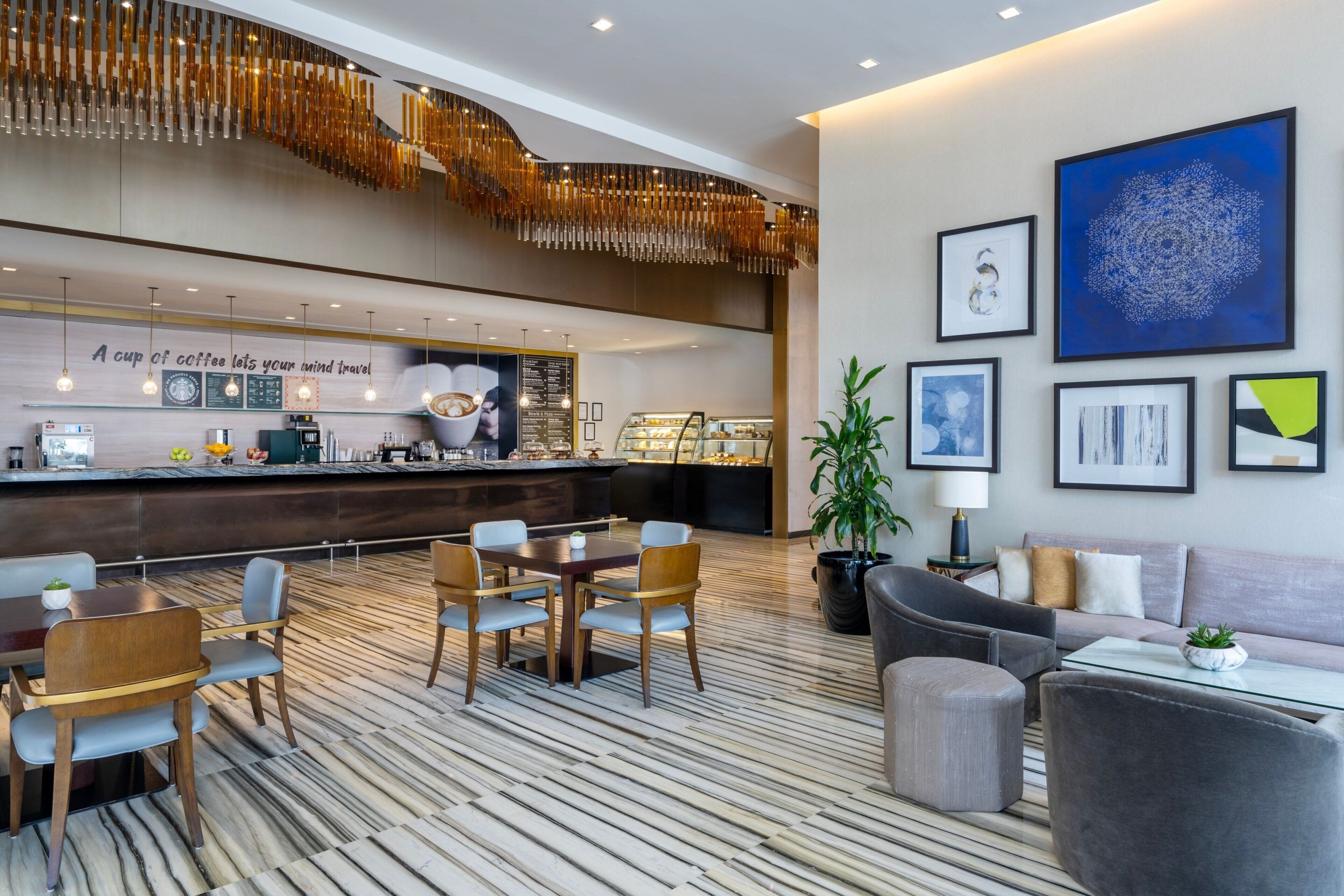 A modern hotel lobby with a coffee bar, seating area, and artwork on the walls.