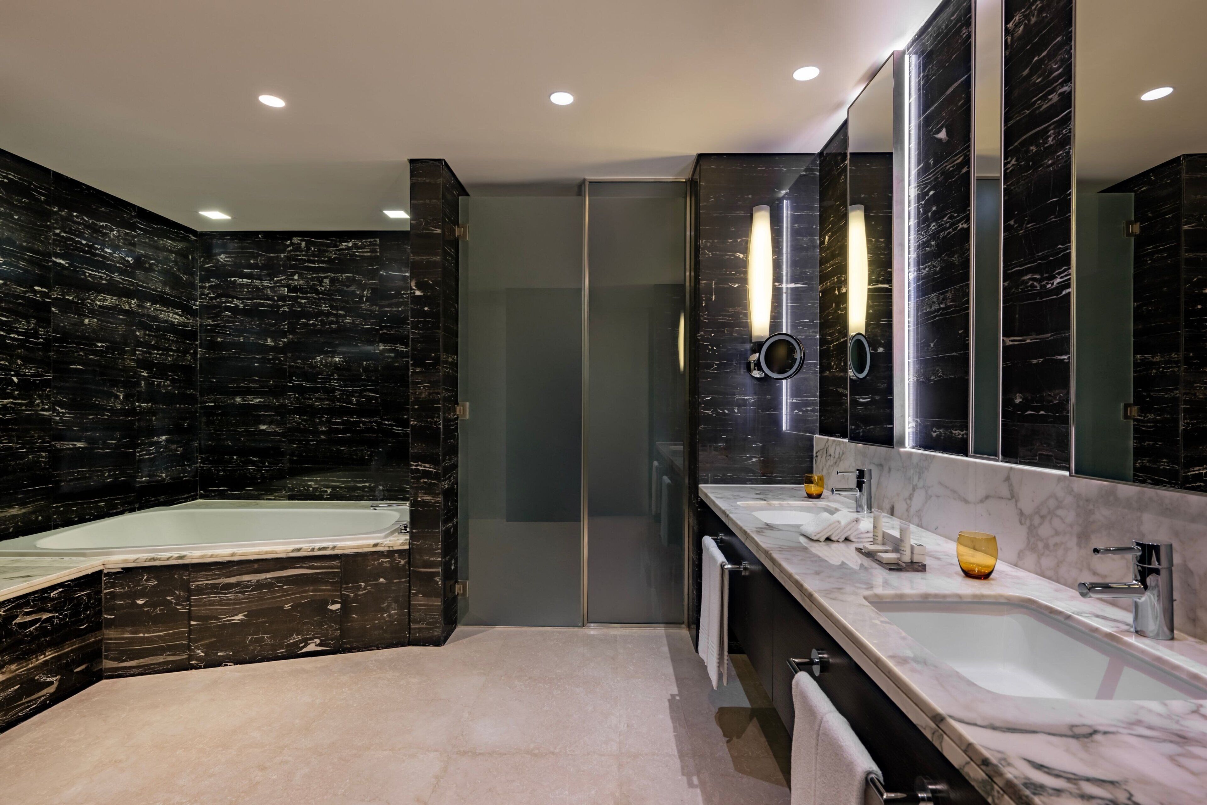 A modern bathroom with a large bathtub, two sinks, and a mirror.