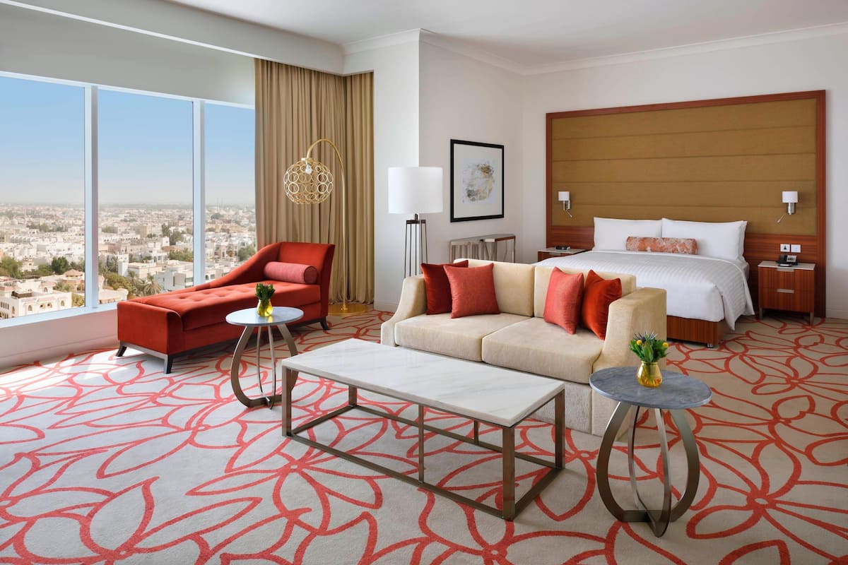 A hotel room with a large bed, two sofas, a coffee table, a side table, and a view of the city.