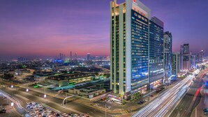 Un hotel moderno de gran altura, con varios pisos, una entrada destacada y vistas de la ciudad al atardecer.