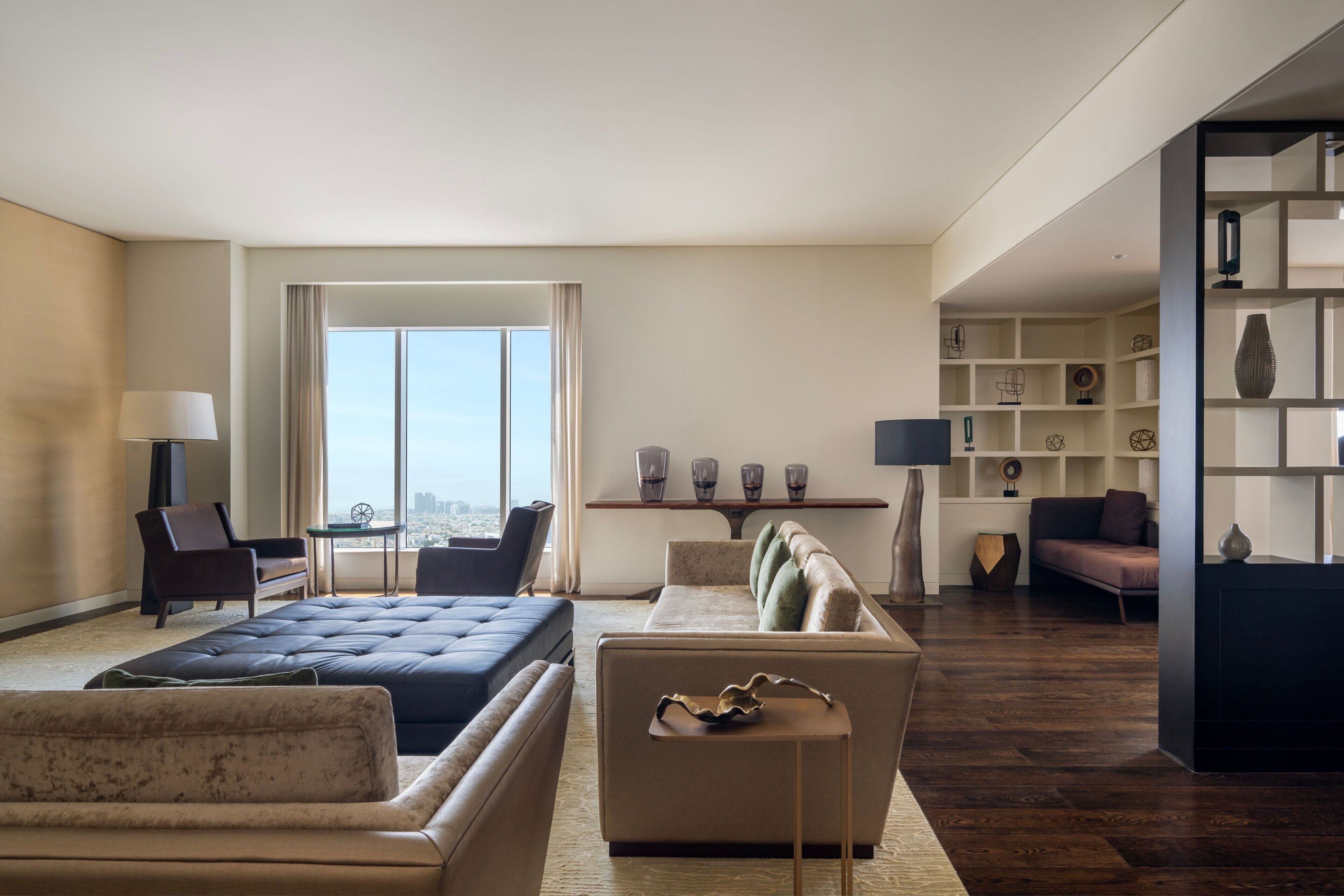 Quarto de hotel moderno com uma cama grande, dois sofás, uma mesa de jantar e vista para a cidade.