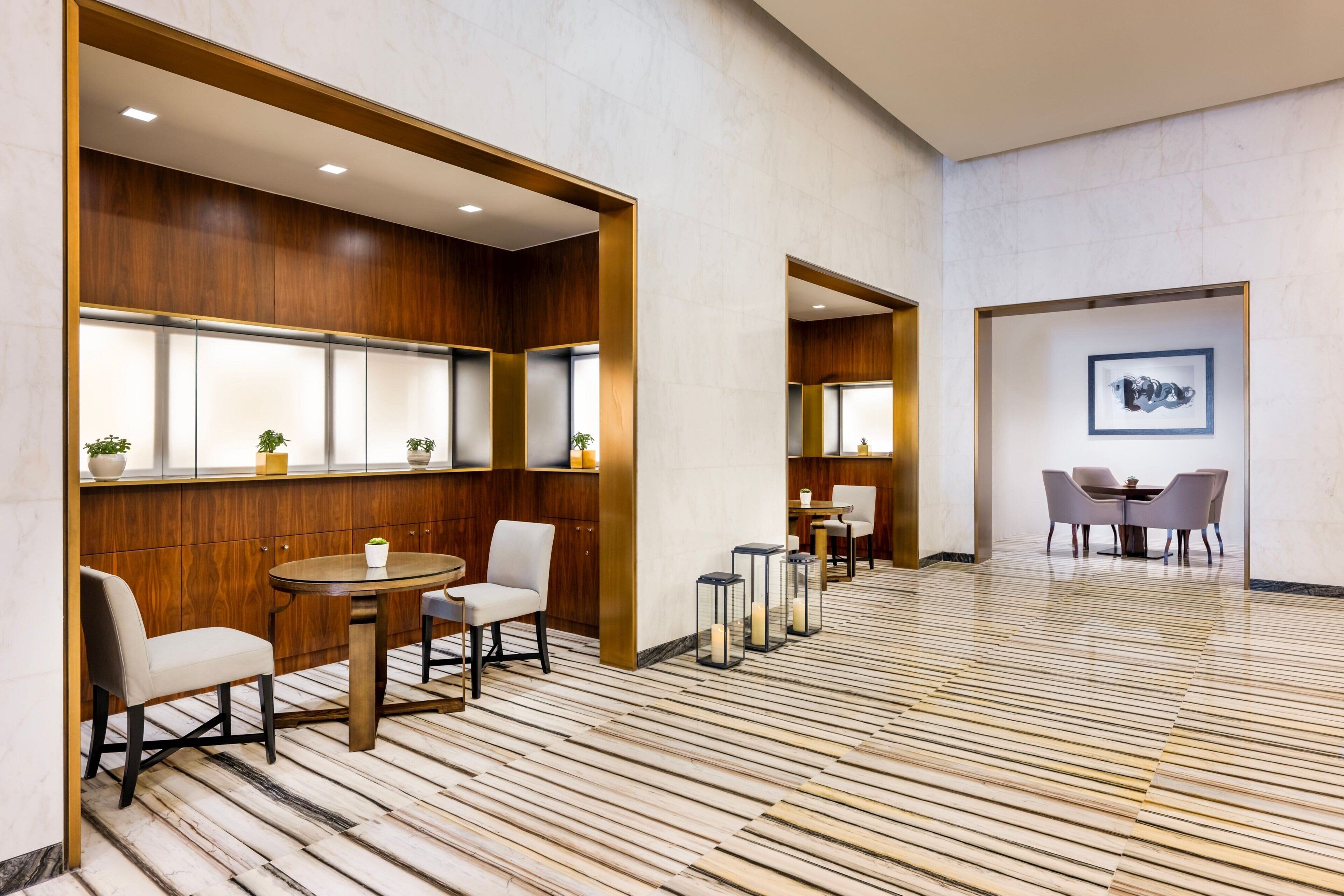 A modern hotel lobby with wooden paneling, a marble floor, and a dining area with tables and chairs.