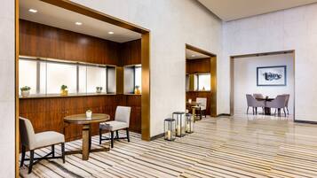 A modern hotel lobby with wooden paneling, a marble floor, and a dining area with tables and chairs.