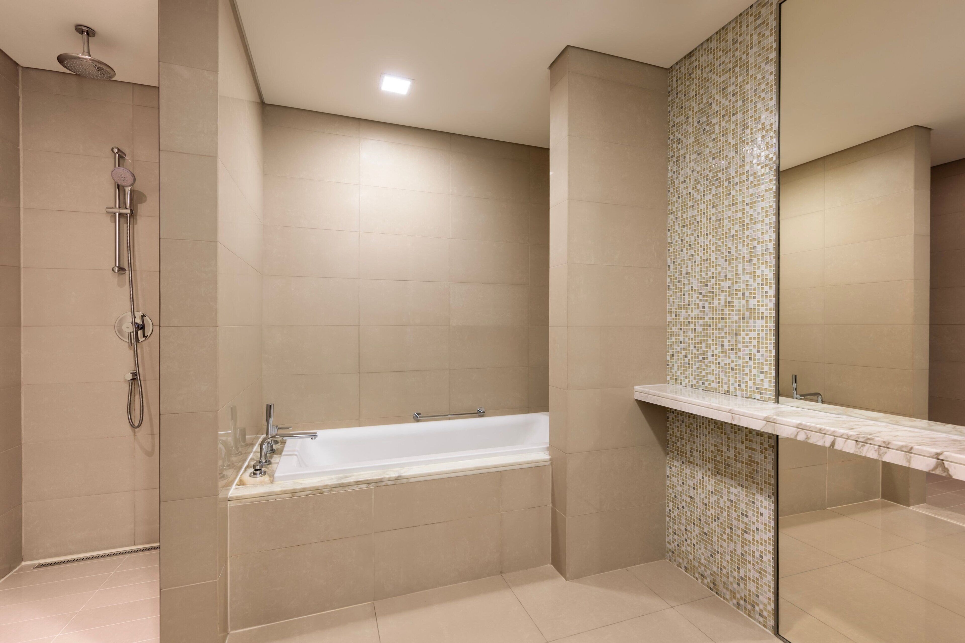 Een moderne badkamer met een badkuip, douche en een betegelde muur met een mozaïekpatroon.