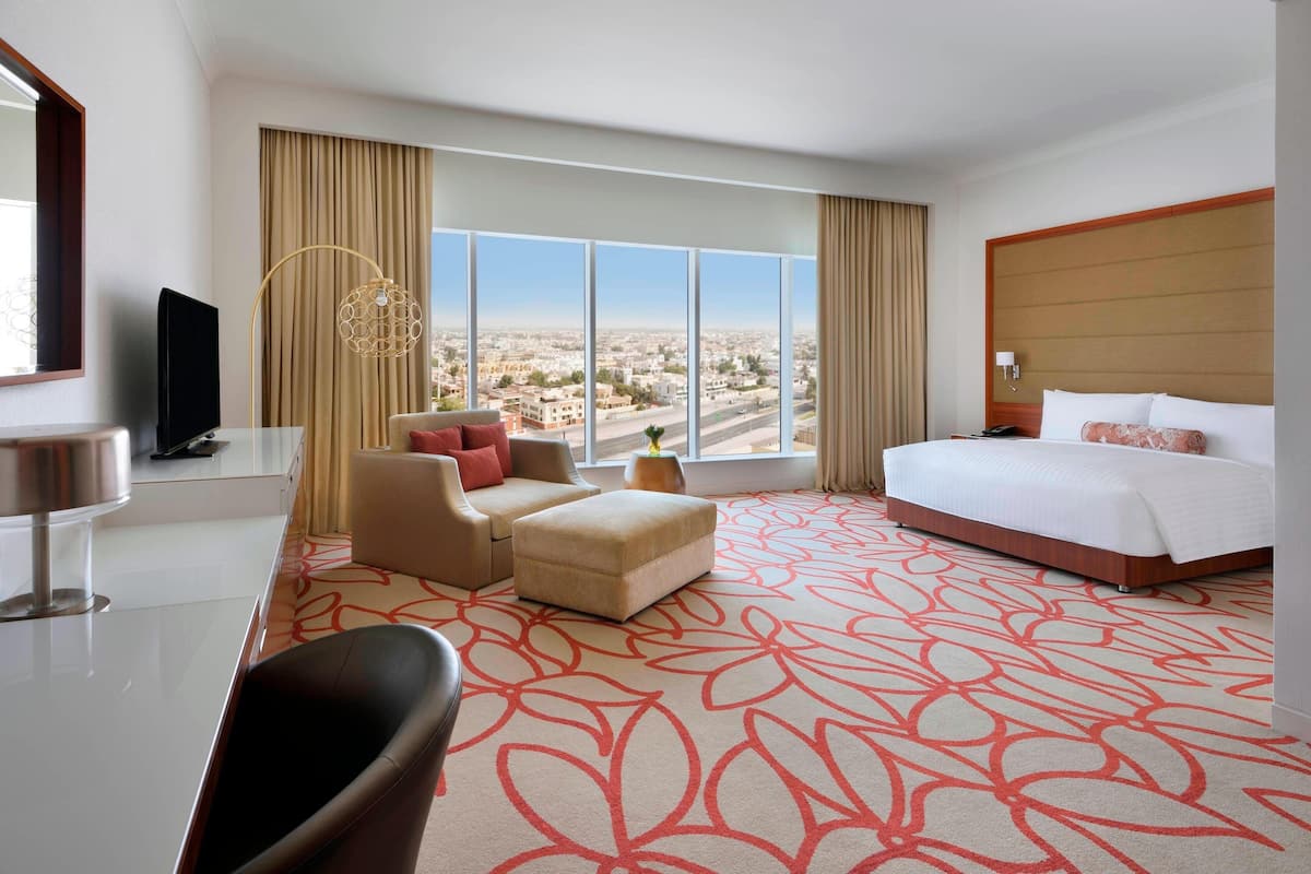 A hotel room with a large bed, a sofa, a desk, and a view of the city.