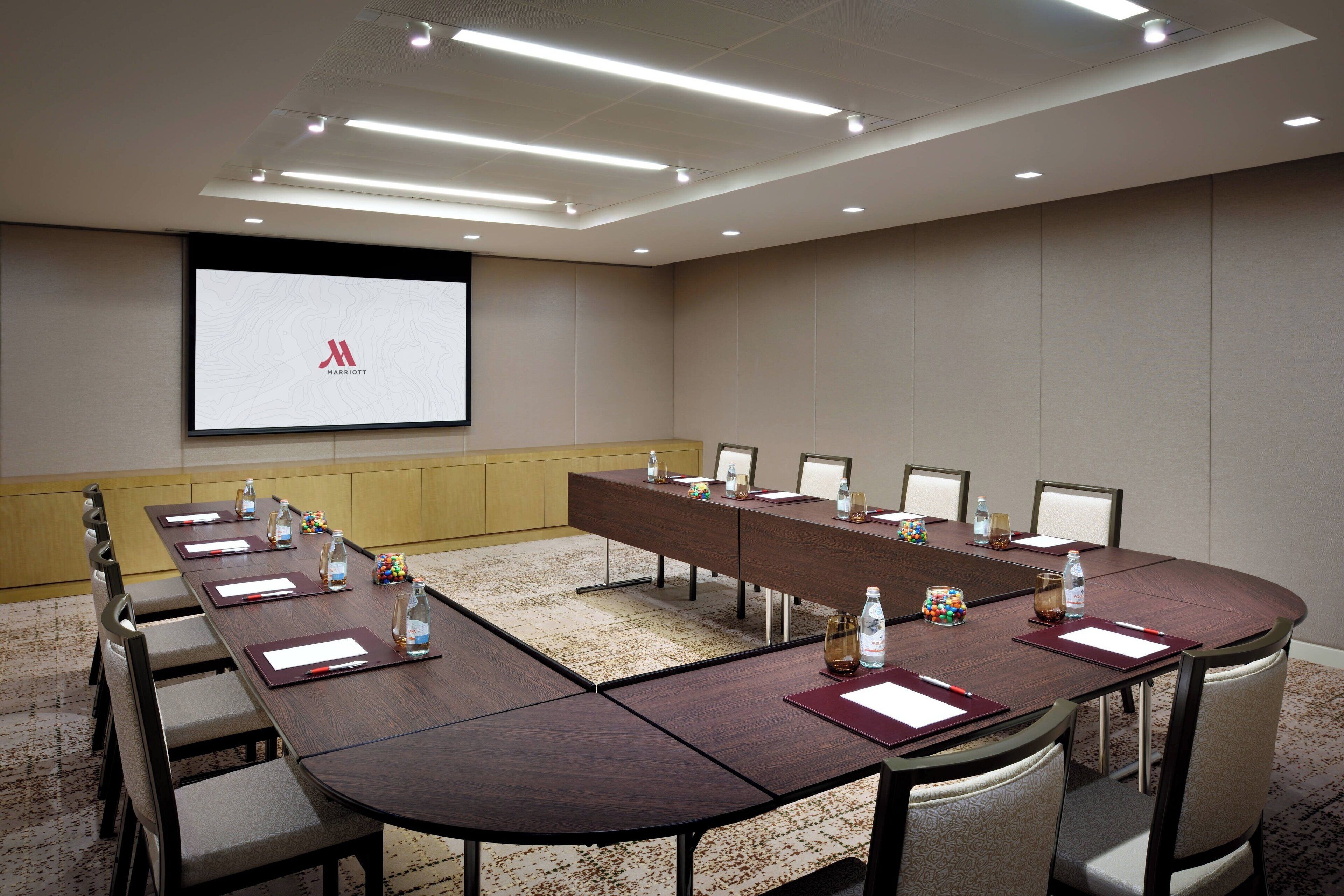 A conference room with a long table, chairs, a projector screen, and a presentation on the screen.