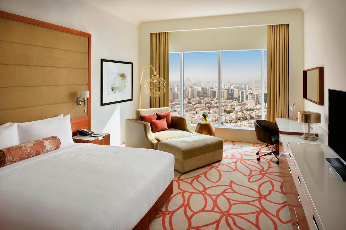 A hotel room with a large bed, a desk, a chair, and a view of the city.