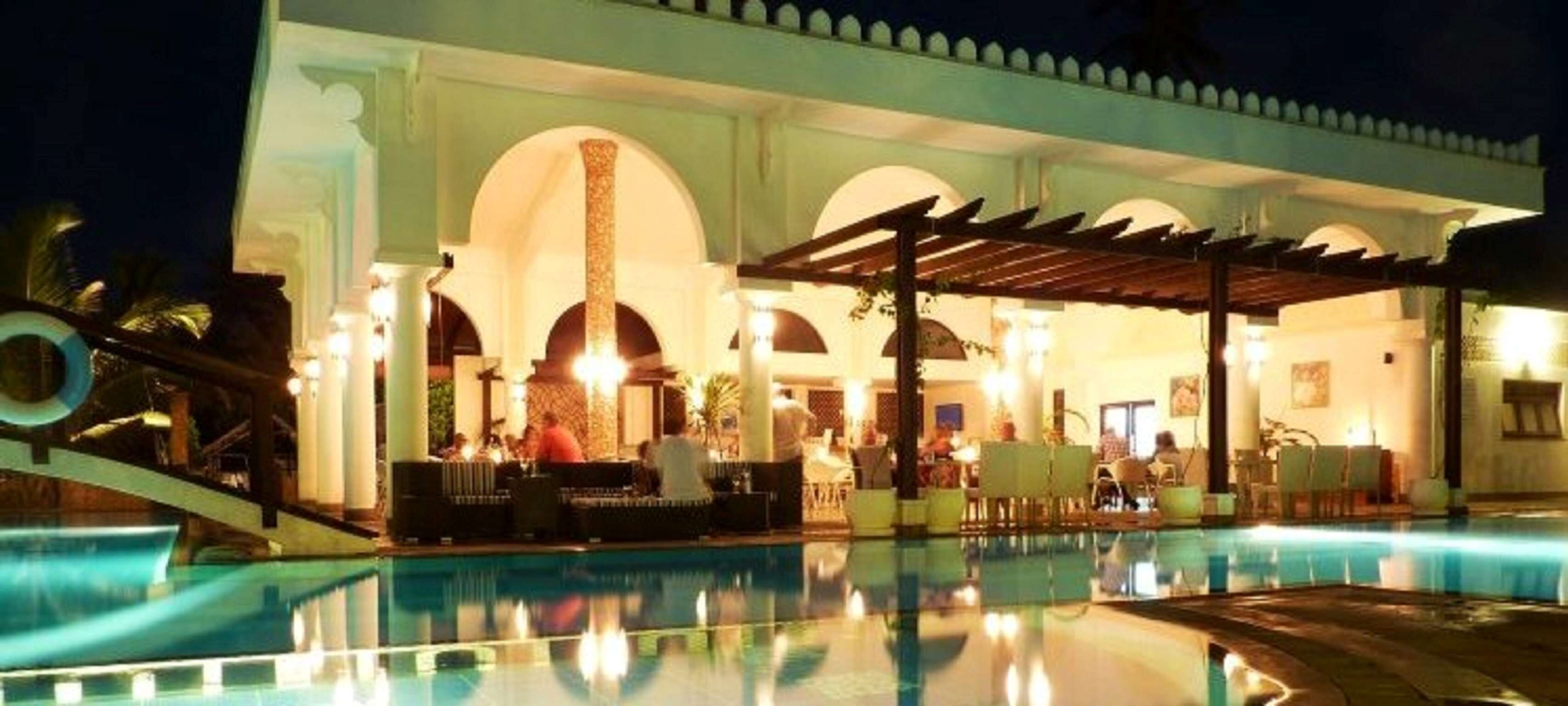 A poolside area with a covered seating area and a building with arches.