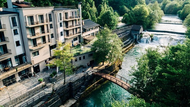 A multi-story hotel with balconies, a river, and a bridge. - Kostelski Buk Hotel (Bihac)