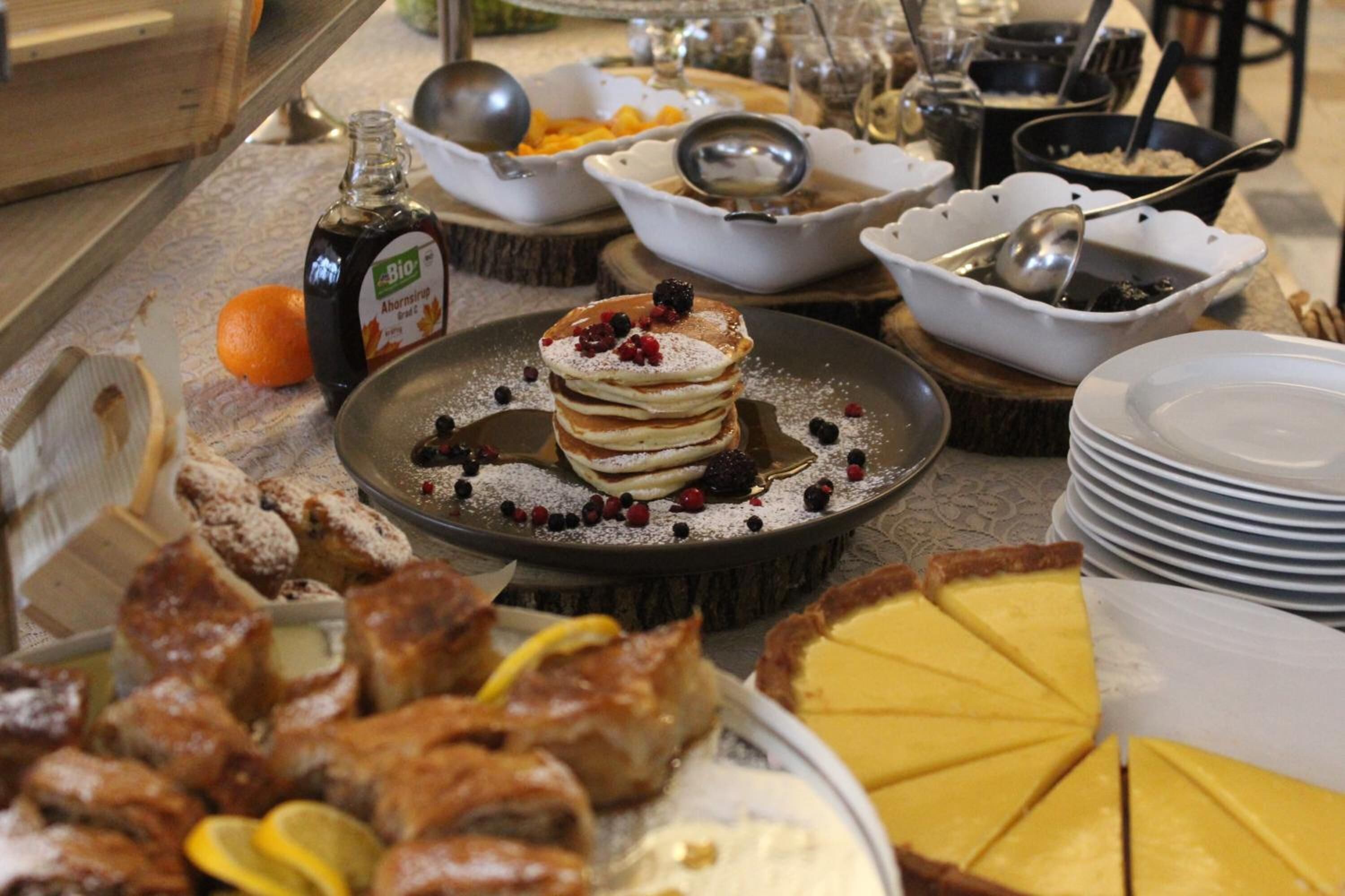 Un buffet proposant divers plats, notamment des crêpes, une tarte et une bouteille de sirop.