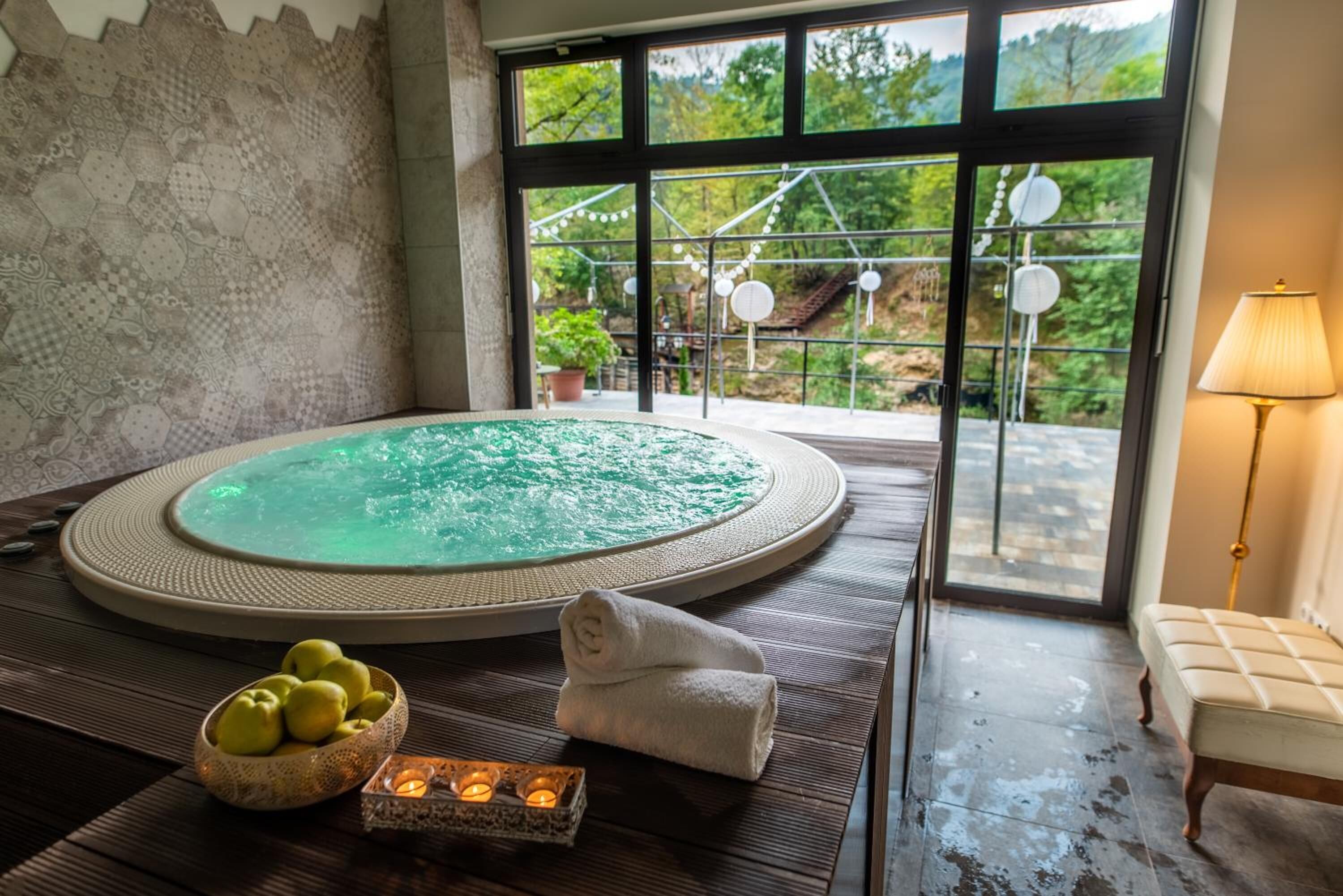 A spa room with a hot tub, a view of greenery, a lamp, and a bowl of apples. - Kostelski Buk Hotel (Bihac)