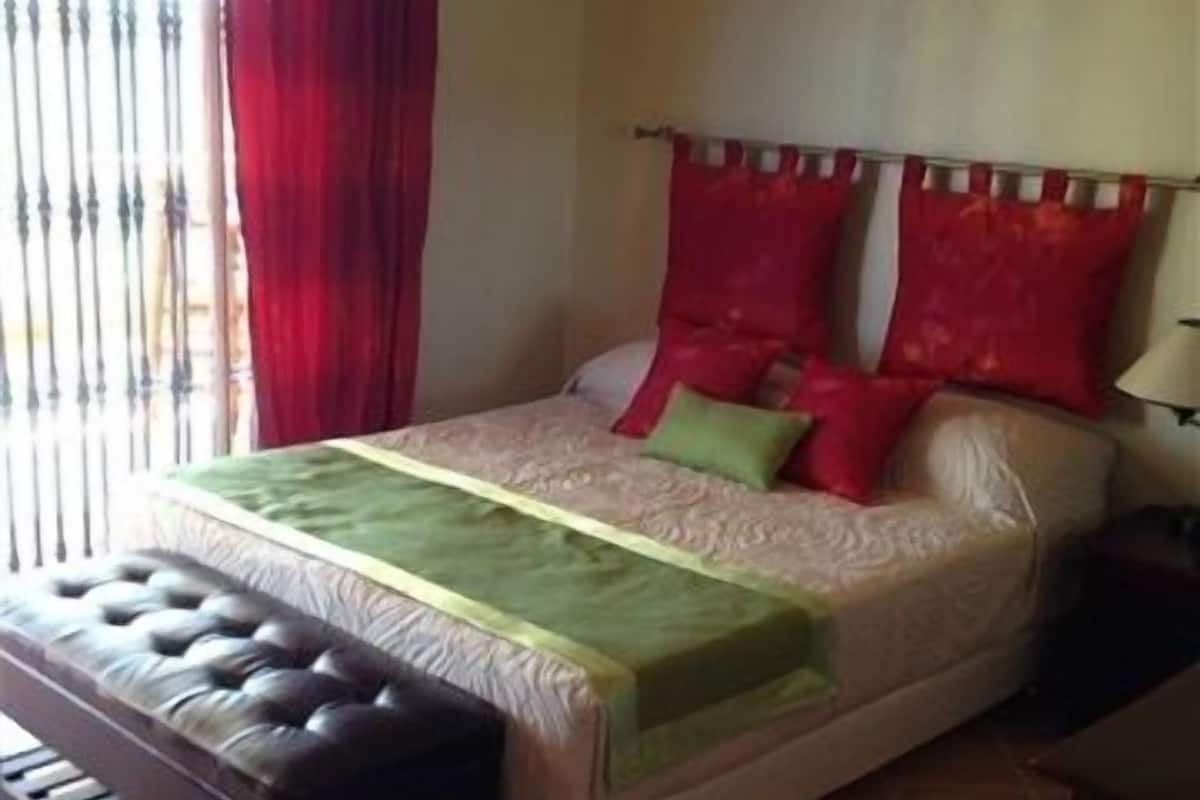 Ein Schlafzimmer mit einem Bett, einer Bank, einer Klimaanlage und einem Fenster mit Vorhängen.