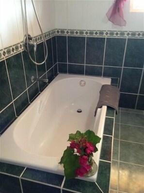 A bathroom with a white bathtub, dark green tiles, and a small potted plant with pink flowers. - Casa Lilly B&B Cabarete (Cabarete)