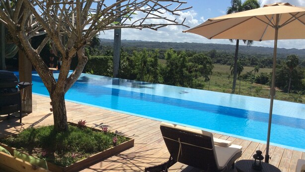 An infinity pool with a wooden deck, lounge chairs, and an umbrella. - Casa Lilly B&B Cabarete (Cabarete)