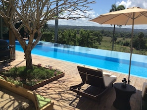An infinity pool with a wooden deck, lounge chairs, and an umbrella. - Casa Lilly B&B Cabarete (Cabarete)