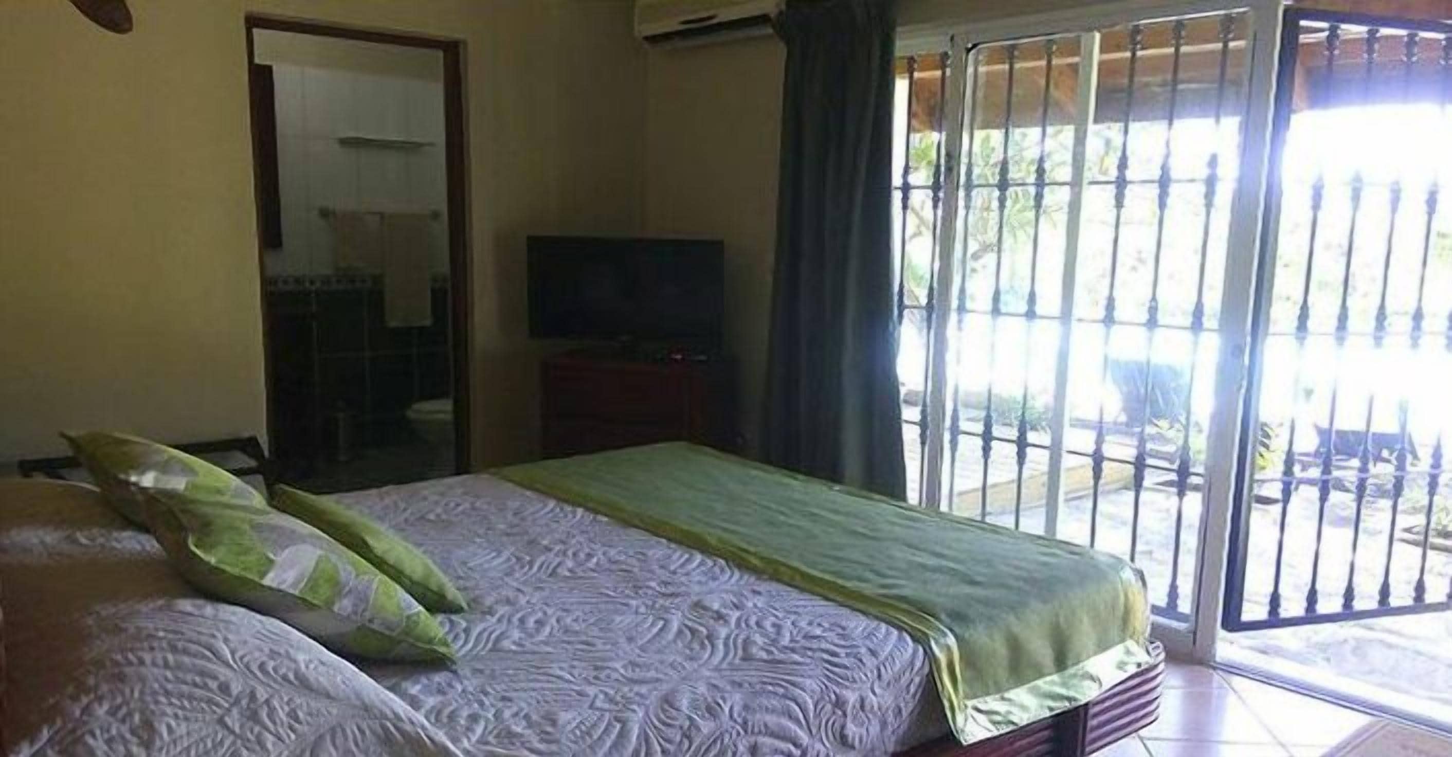 Ein Schlafzimmer mit Bett, Fernseher und Blick durch ein Fenster mit einem Metallgitter.