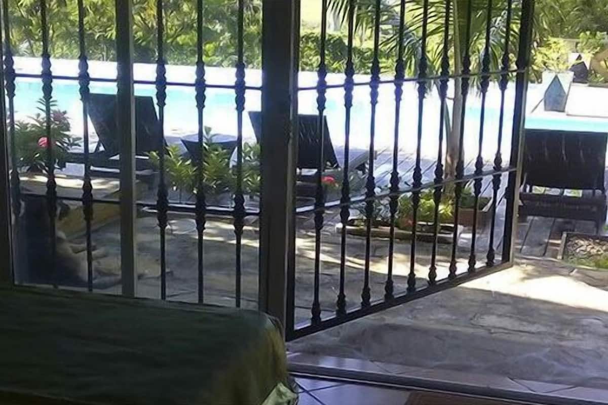 Blick durch ein Metallgitter auf einen Poolbereich mit Liegestühlen und einer kleinen Bühne.