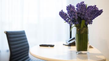 Una mesa redonda con un jarrón de flores moradas, un control remoto y un teléfono encima.