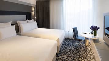 A hotel room with two beds, a desk with a chair, a TV, and a window with curtains.
