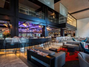 A modern bar area with a high ceiling, bar stools, and a seating area with sofas and tables.