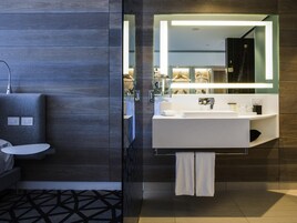 Un baño moderno con un espejo grande, un lavamanos blanco y una ducha con mampara de vidrio.