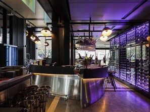 A modern bar area with a central counter, multiple hanging lights, and a wine rack along the wall.