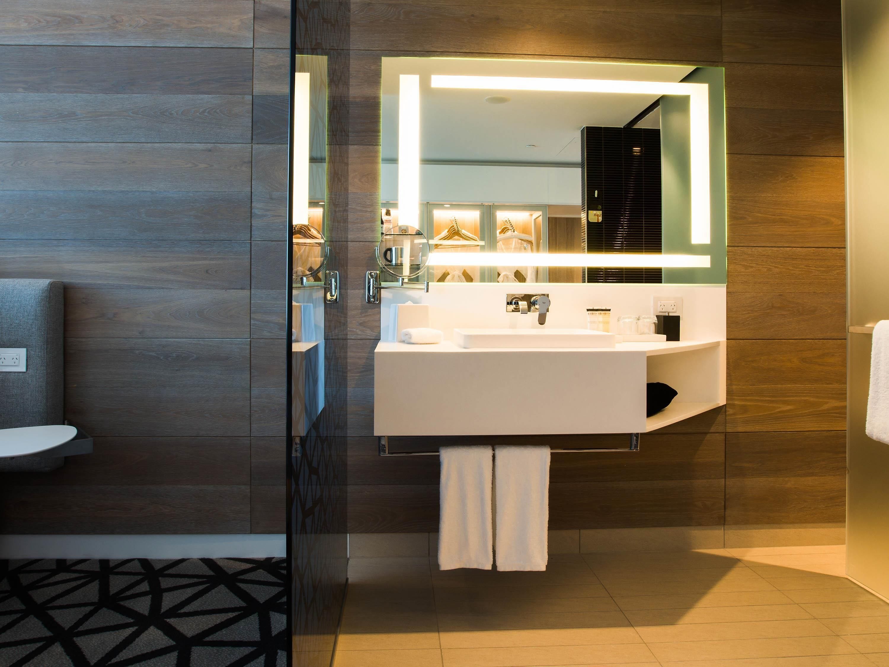 A modern bathroom with a large mirror, white sink, and towel rack.
