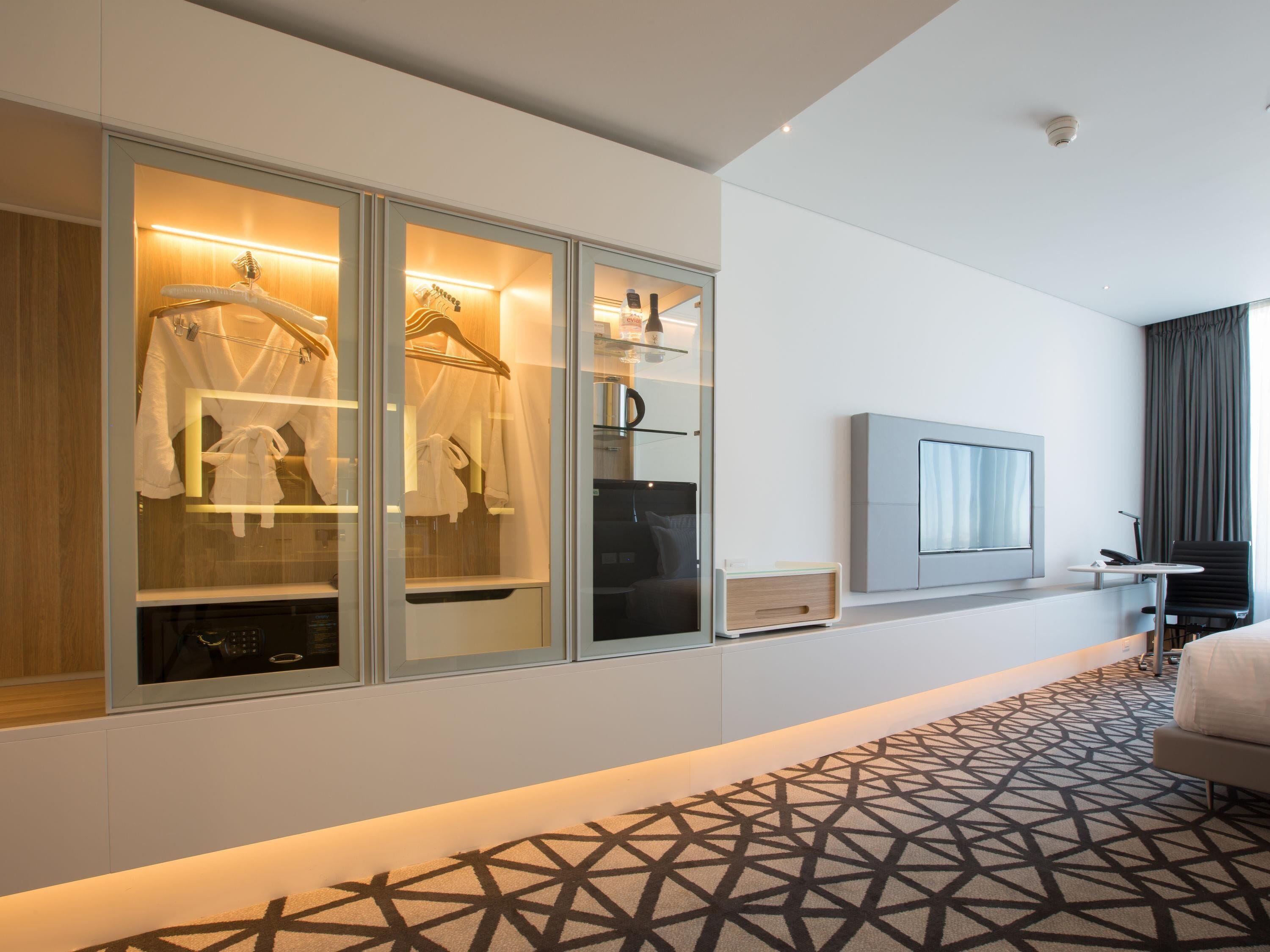 A hotel room with a large wardrobe, a flat-screen TV, a bed, and a patterned carpet.