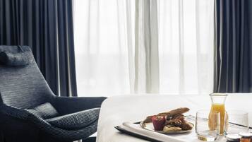 A hotel room with a bed, a chair, breakfast tray, and a window with curtains.