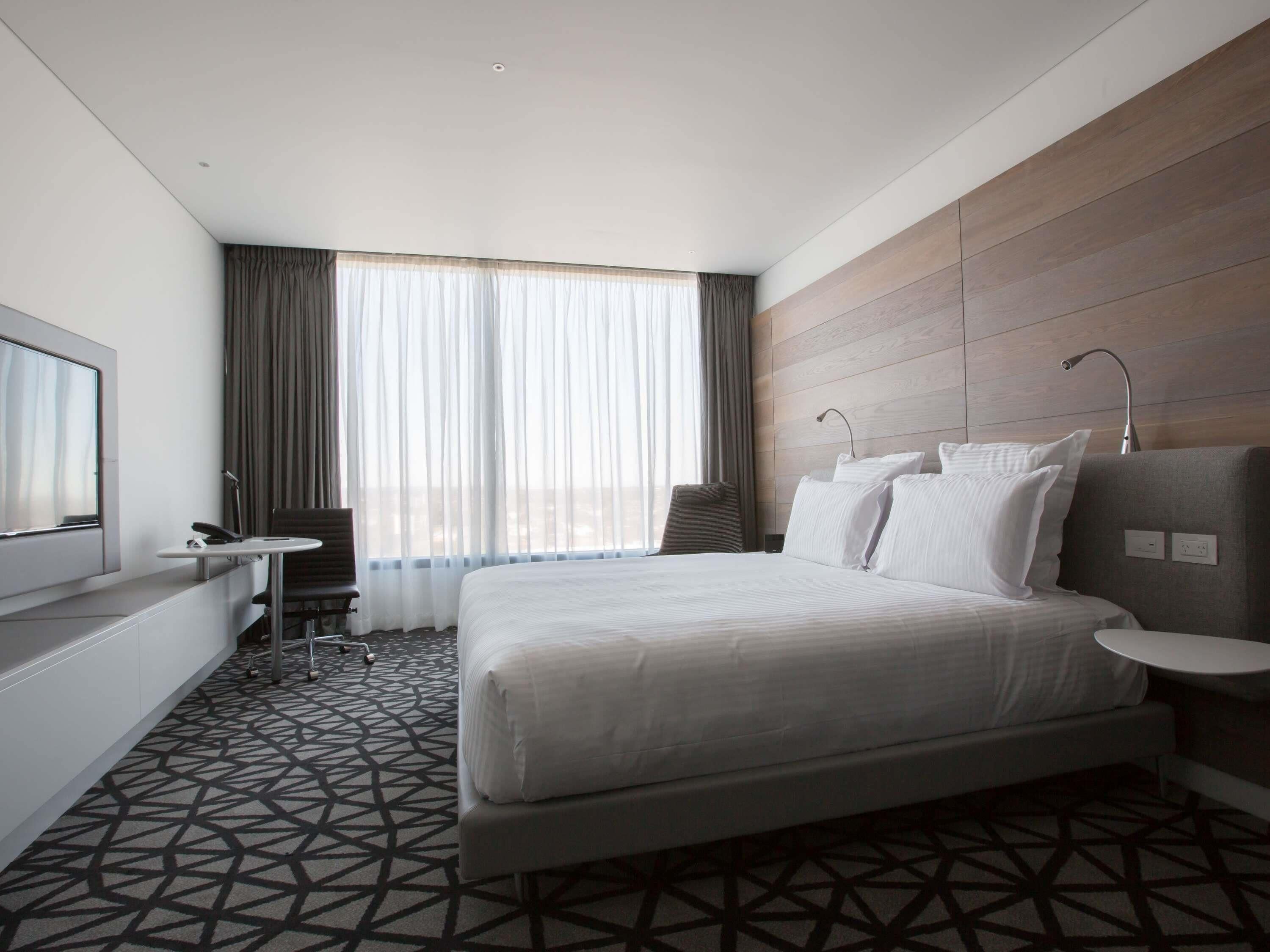 A modern hotel room with a large bed, a desk, and a TV.