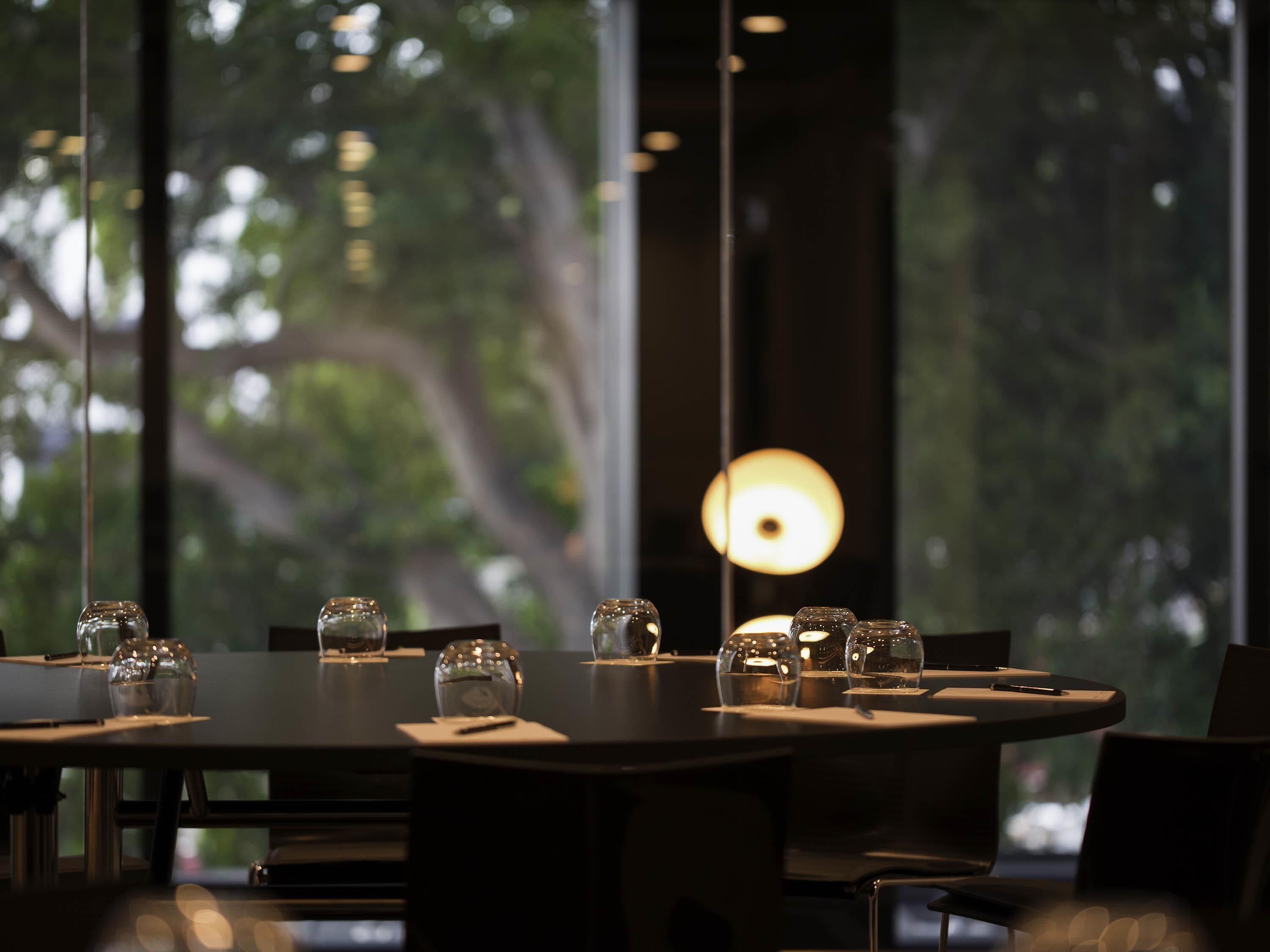 Un comedor con mesas redondas, vasos de vidrio transparente y lámparas colgantes.