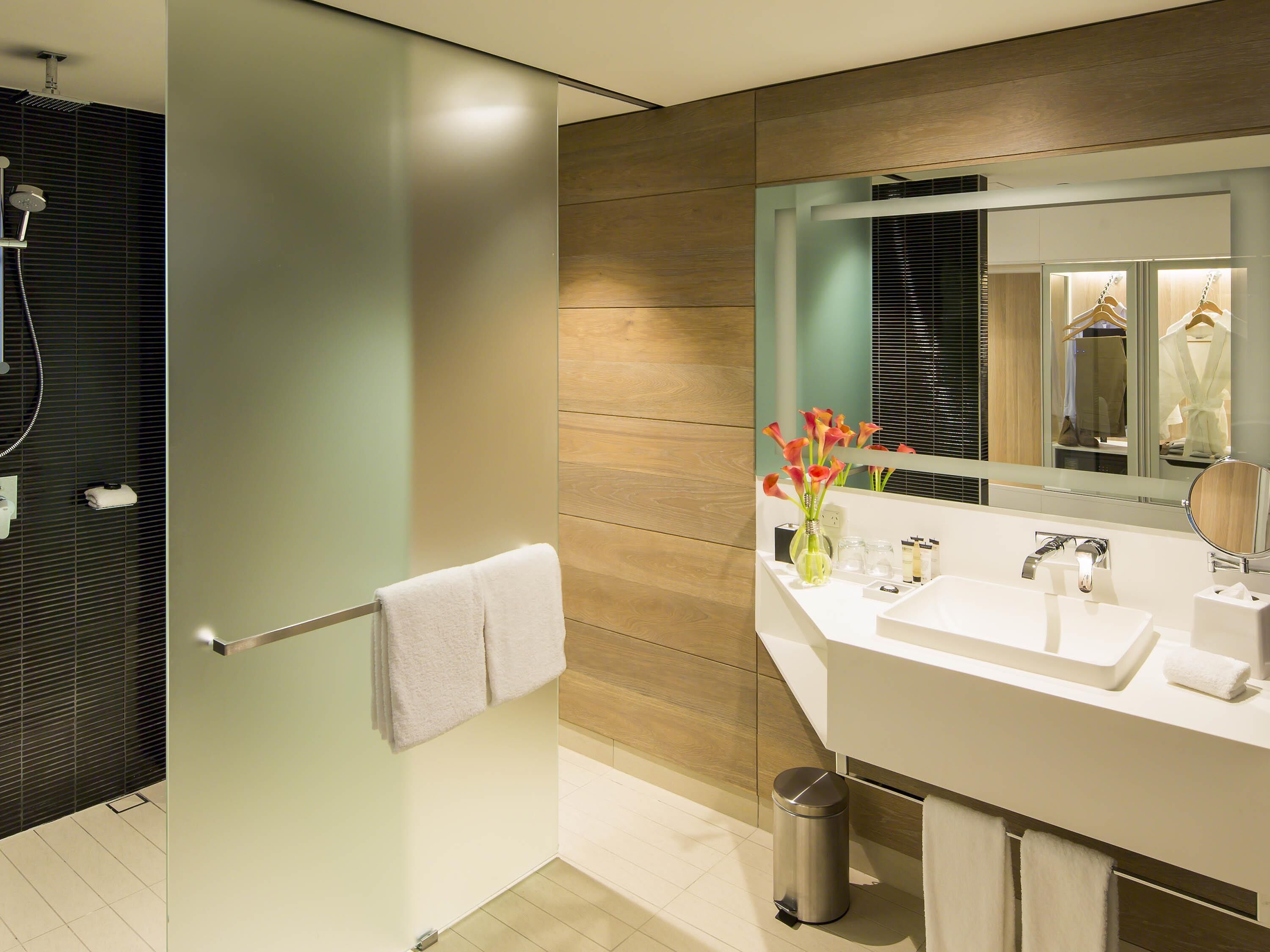 A modern bathroom with a glass shower enclosure, a white sink with a mirror, and a vase with flowers.