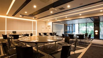 A modern conference room with round tables, black chairs, and a glass partition wall.
