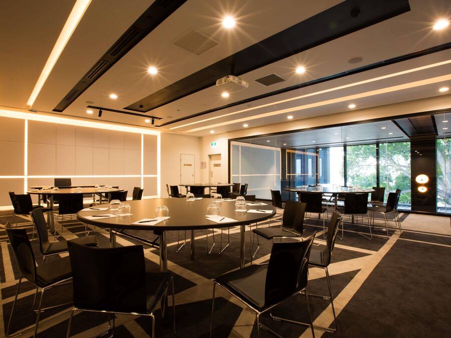 A modern conference room with round tables, black chairs, and a glass partition wall.