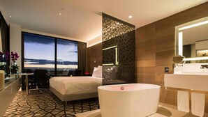 A modern hotel room with a large bed, a round bathtub, and a bathroom with a large mirror. - Pullman Sydney Airport (Mascot)